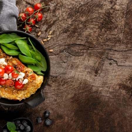 Ketaus keptuvė su paruoštu patiekalu ant medinio virtuvės stalo, pabrėžianti jos patvarumą ir tolygų šilumos paskirstymą.